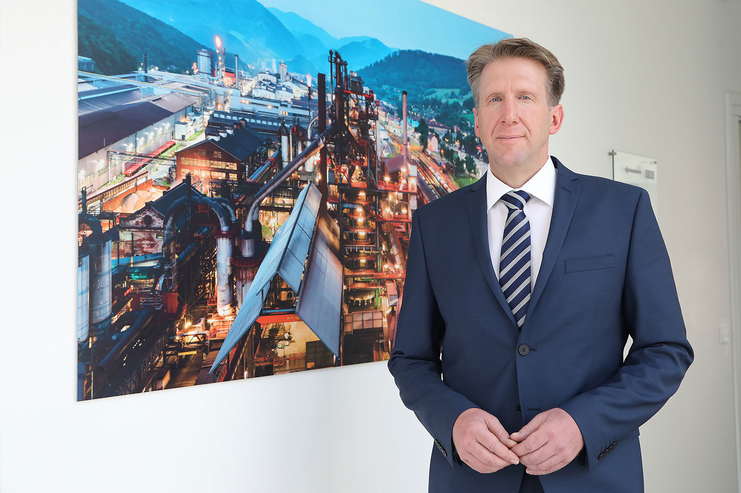 Gerhard Schuster, Managing Director responsible for production at voestalpine Stahl Donawitz GmbH, standing before a—still—representative painting of his site.