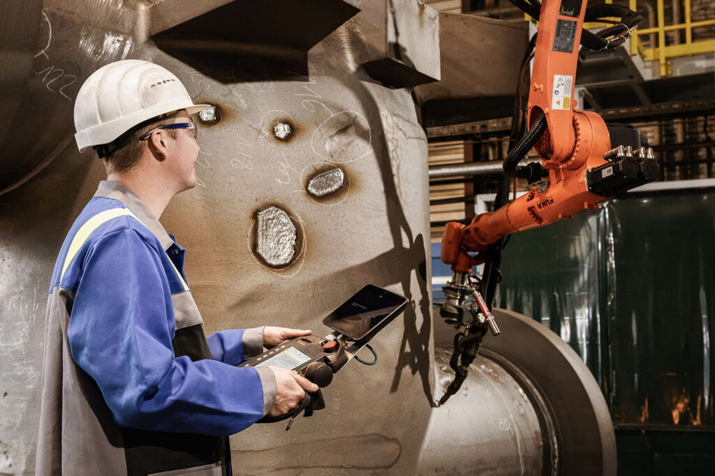 A voestalpine employee operates a robot welding system