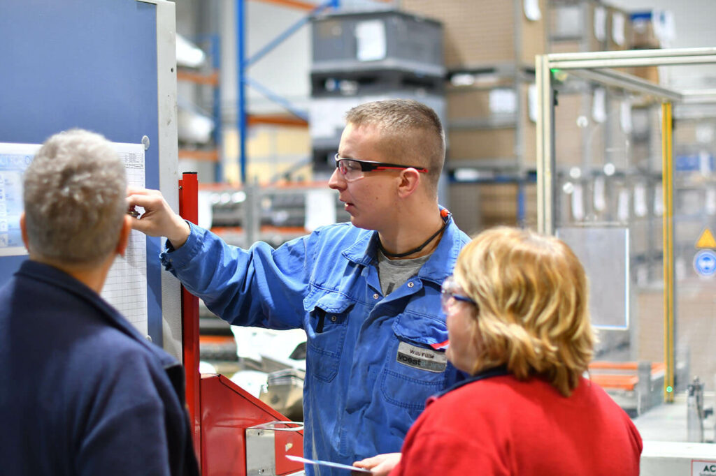 Willi conducts a training session and writes information onto a list, two employees watching him