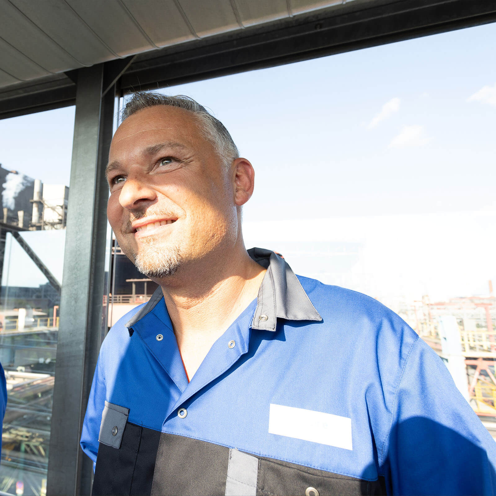 Markus, a vosetalpine employee, wears blue and black work clothes and smiles as he looks past to the left of the camera