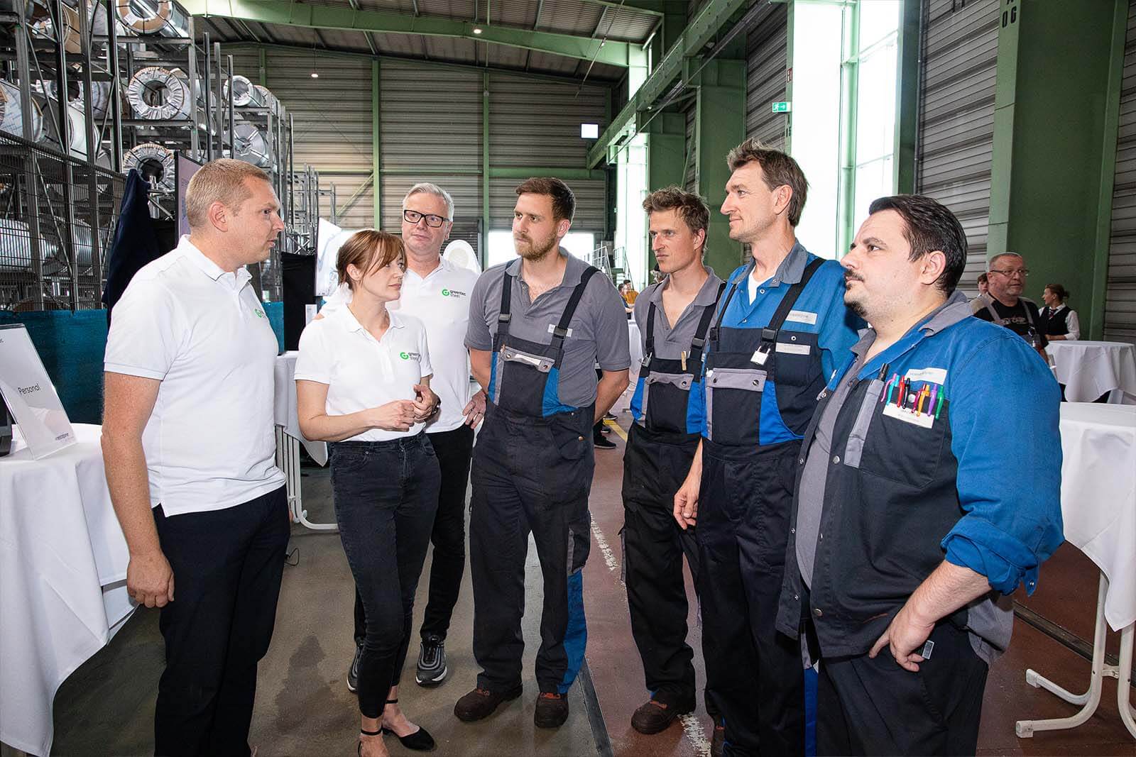 four voestalpine employees in work clothes and one female and two male employees wearing greentec steel shirts