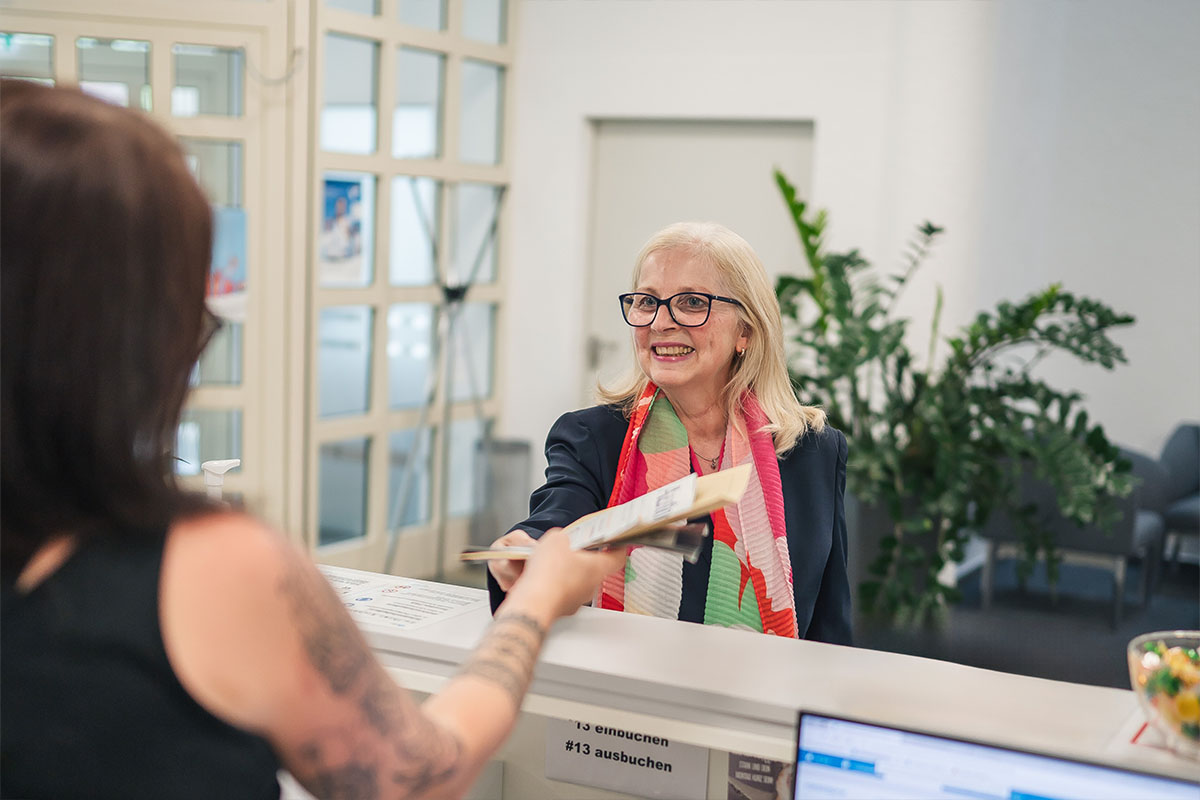 Susanne Gutbrod nimmt lächelnd Dokumente entgegen von einer Kollegin