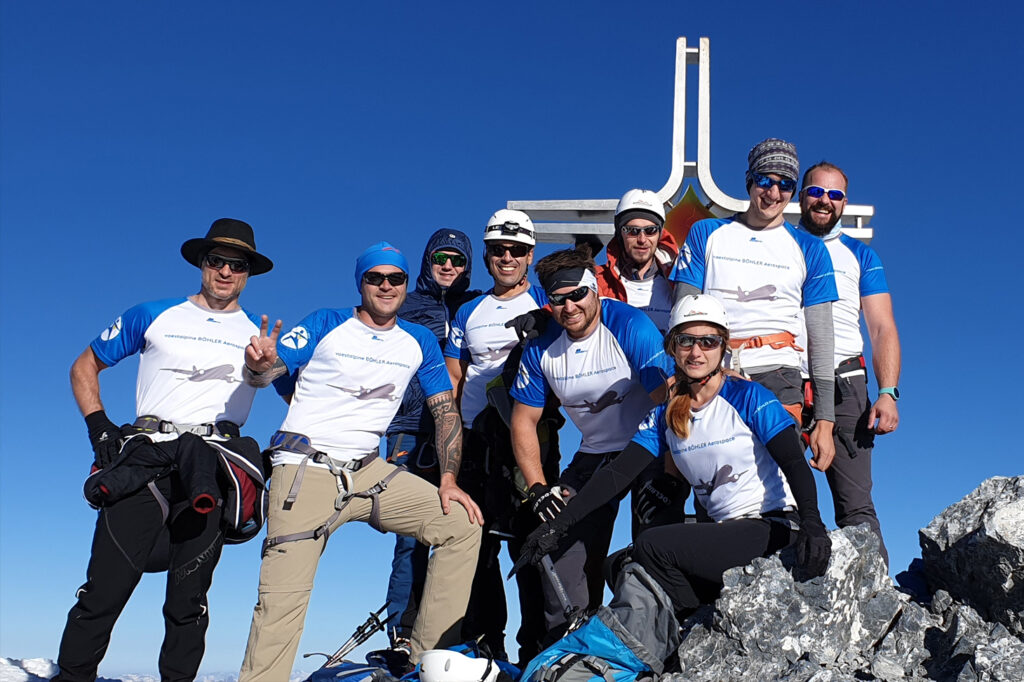 Gruppenfoto der voestalpine Mitarbeiterinnen und Mitarbeiter am Gipfel vor dem Gipfelkreuz