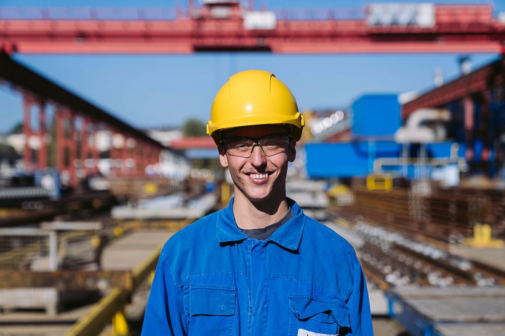 Portrait photo of voestalpine employee Lukas K with work clothes, safety helmet and goggles