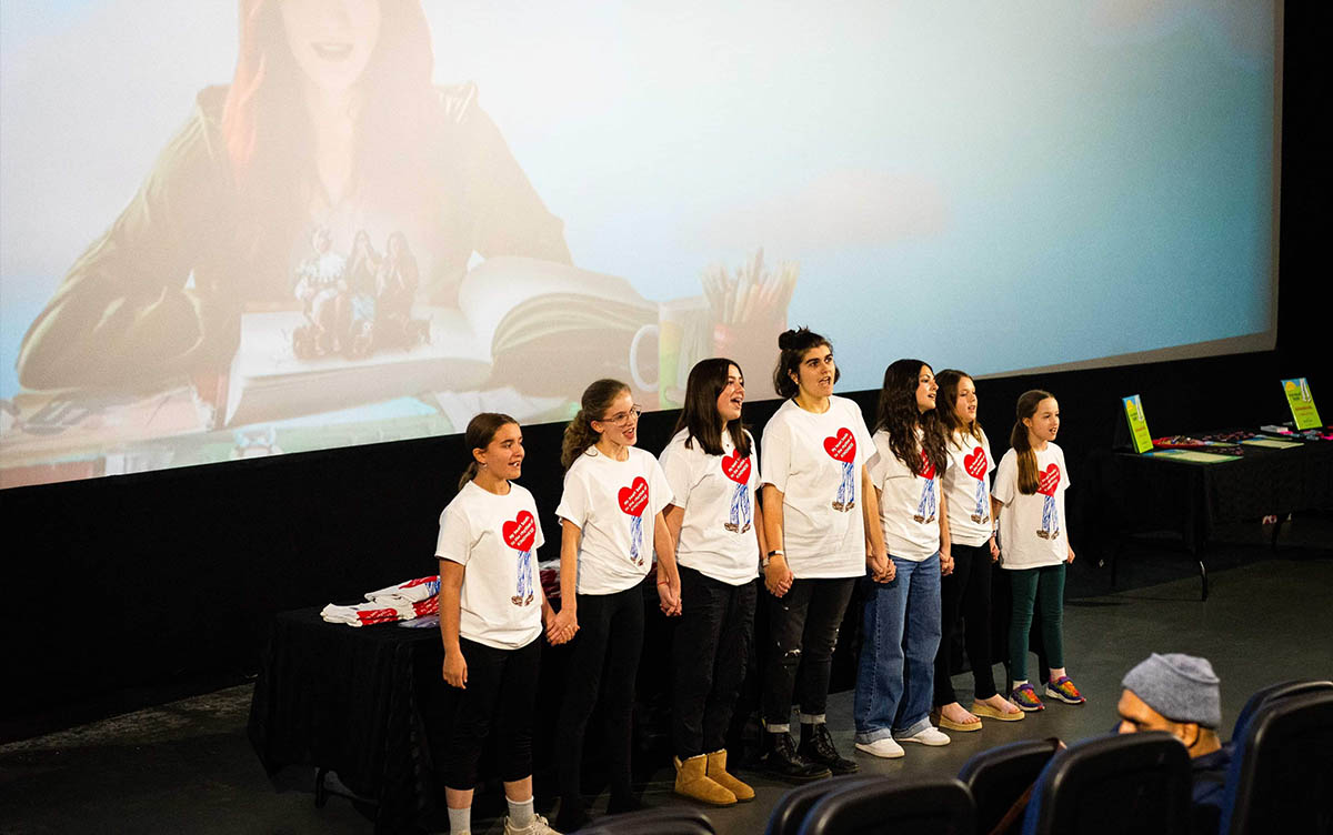 7 Kinder stehen vor der Leinwand und singen bei der Vorführung des Films über Nelson The Giant