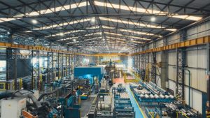 Innenansicht der modernen voestalpine Produktionshalle in Brasilien mit Maschinen, Anlagen, Werkstücken und Mitarbeitenden in Schutzkleidung während des laufenden Betriebs.