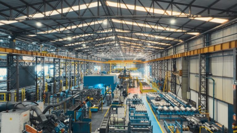 Innenansicht der modernen voestalpine Produktionshalle in Brasilien mit Maschinen, Anlagen, Werkstücken und Mitarbeitenden in Schutzkleidung während des laufenden Betriebs.