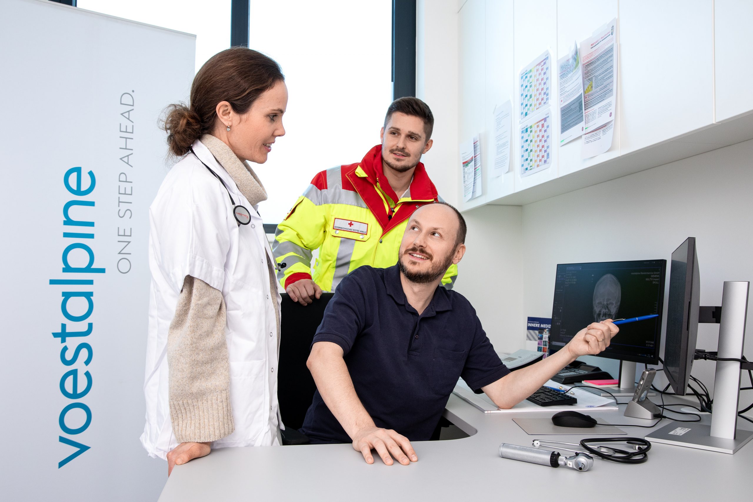 Pippa P., ein Rettungssanitäter und Mitarbeiter besprechen eine Schädel-Röntgenaufnahme am Computer in der Klinik der voestalpine