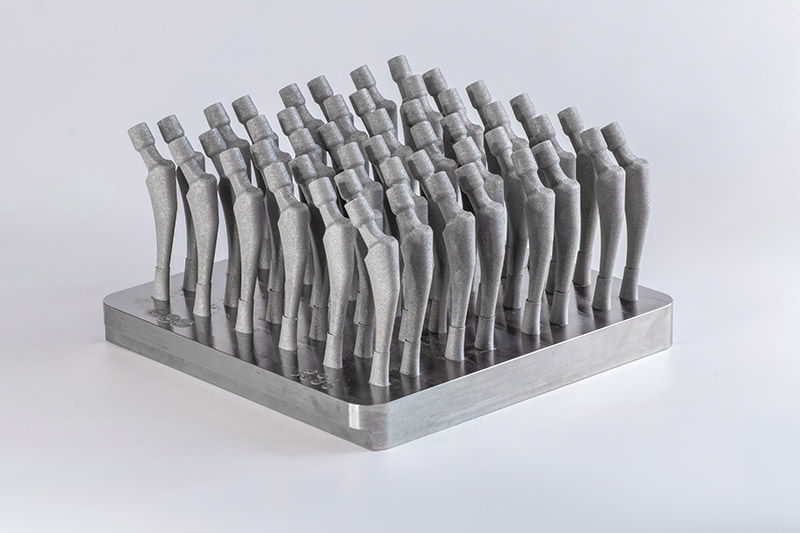 Multiple metallic implant or precision components produced on a manufacturing plate using an industrial 3D printing process.
