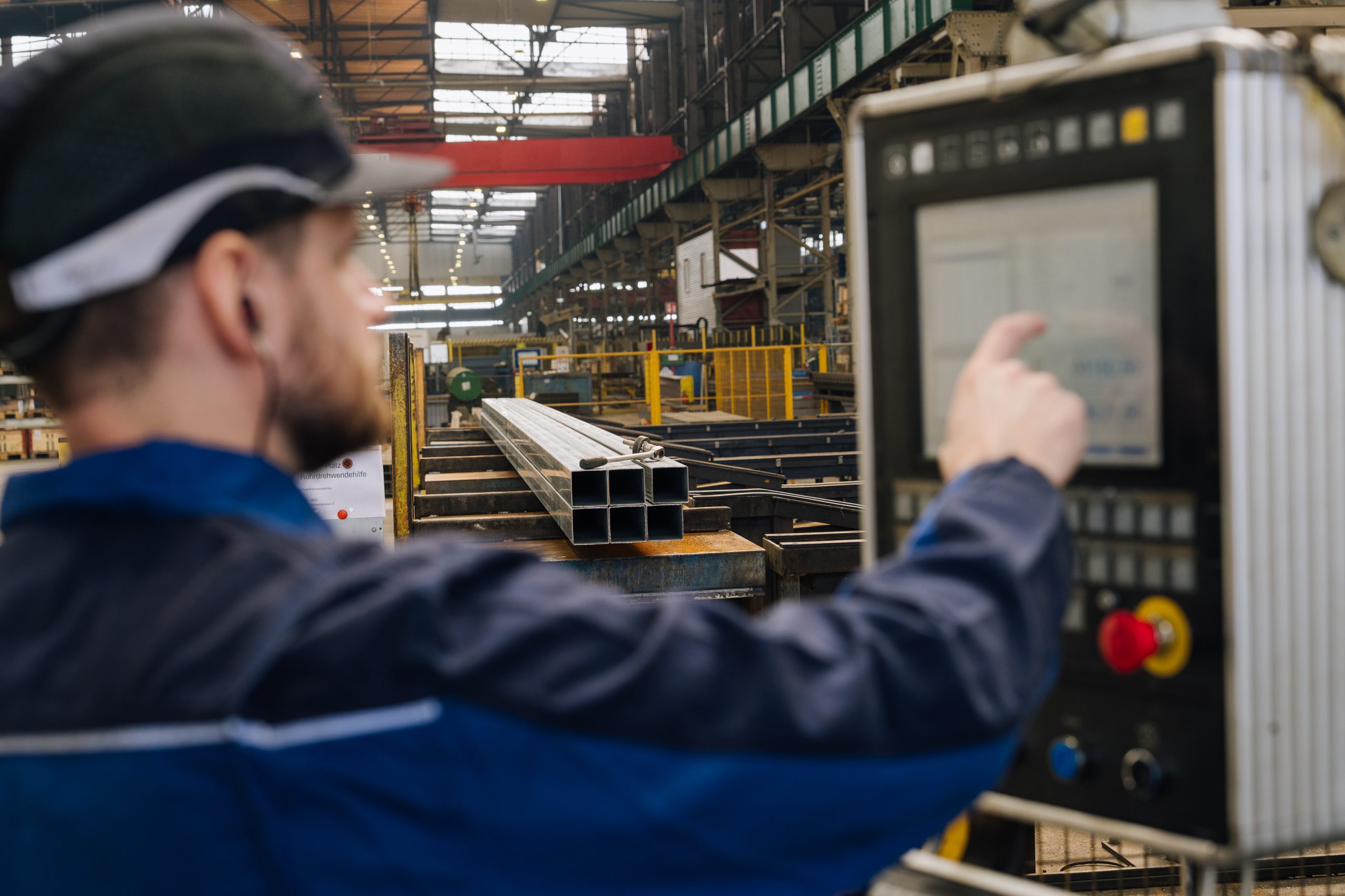 Daniel in Arbeitskleidung steuert eine Fertigungsanlage über einen digitalen Touchscreen und überwacht den Produktionsprozess.