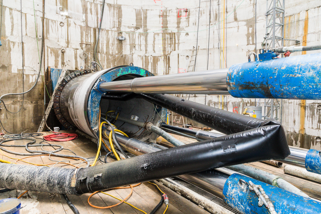 Microtunnel-Baustelle mit großem Vortriebsrohr, Hydraulikzylindern und technischen Leitungen in einer Betonschachtanlage.
