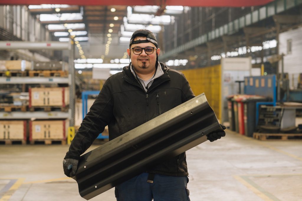 Employee presents a steel profile for road safety products in a modern metal processing manufacturing environment.