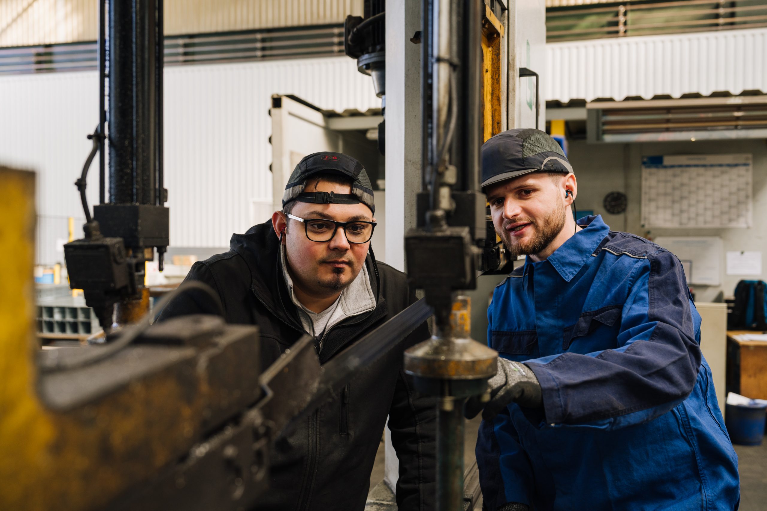 Two voestalpine employees collaborate at an industrial machine to ensure precise manufacturing processes in metal processing.