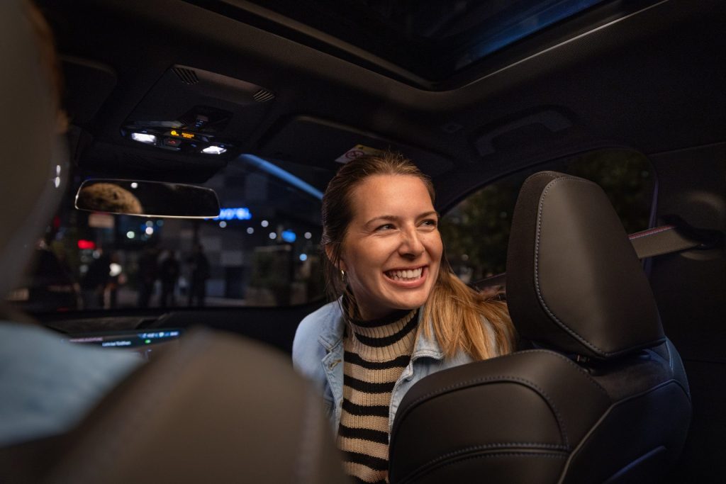 Eine lächelnde Frau sitzt bei Nacht im Auto und blickt nach hinten.