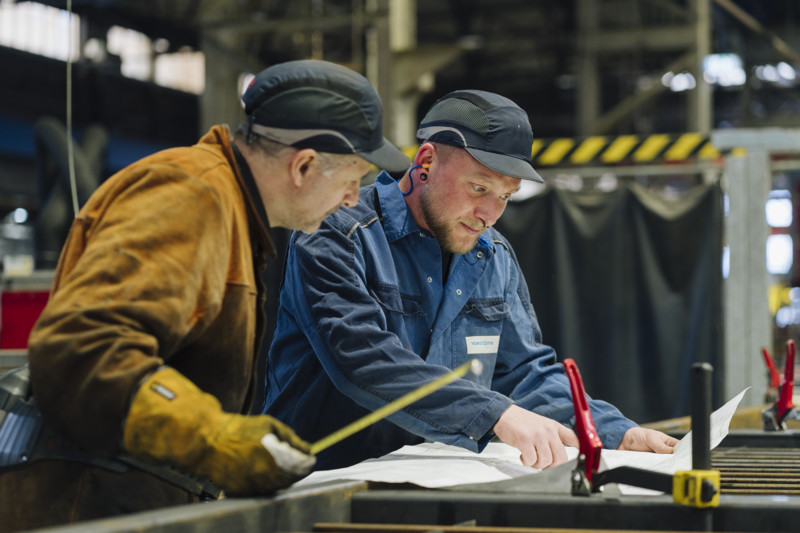 Wolfgang and his college reviewing technical documents and measurements together at a workstation in the production hall.