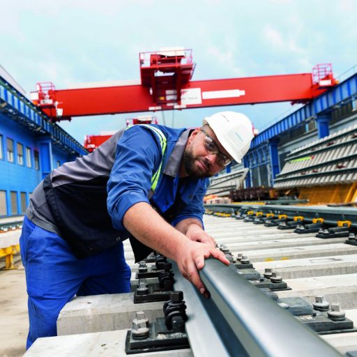 Mitarbeiter mit Schutzhelm kontrolliert eine montierte Schiene auf einer Test- und Produktionsanlage für moderne Bahninfrastruktur.