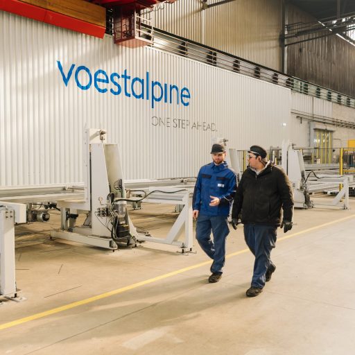 Two employees in workwear discuss production processes in a modern manufacturing hall equipped with automated machinery.