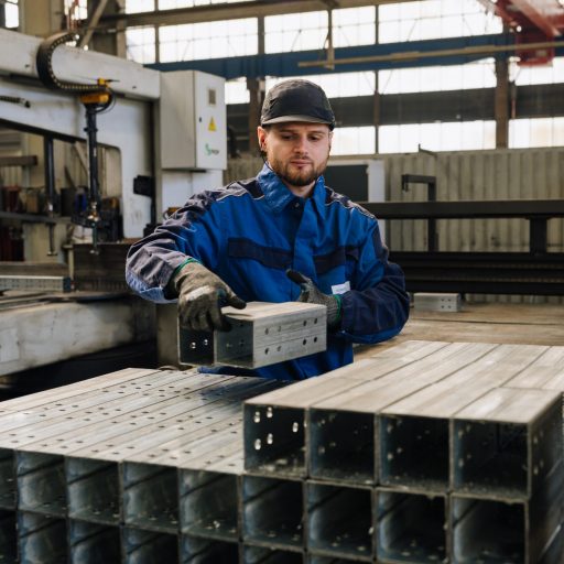 Daniel prüft Stahlprofile und Qualitätsmerkmale in der Metallverarbeitung innerhalb einer modernen Produktionshalle.