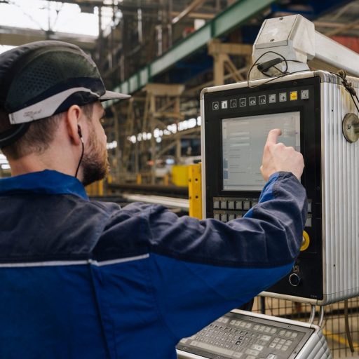 Mitarbeiter mit Schutzhelm und Arbeitskleidung steuert eine Produktionsanlage über einen Touchscreen in einer modernen Industrieumgebung.