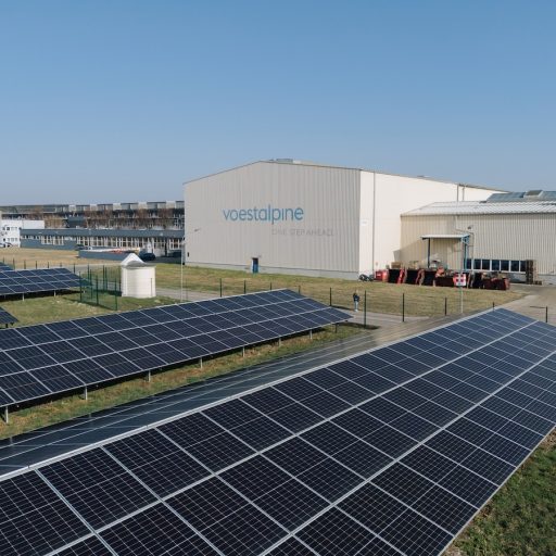 Photovoltaikanlage vor den Produktionshallen von voestalpine Krems unter blauem Himmel. Auf einer Werkshalle ist zu lesen voestalpine - one step ahead
