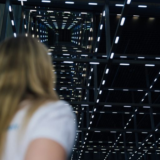 Besucherin blickt in den beleuchteten Grid der voestalpine Stahlwelt, eine begehbare Stahlkonstruktion mit zahlreichen LED-Lichtpunkten.
