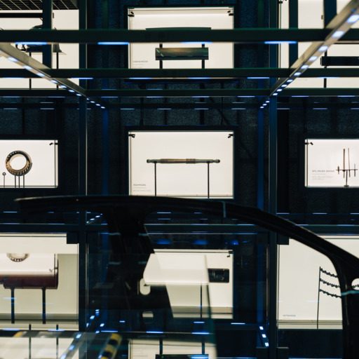 Ausstellungsbereich der voestalpine Stahlwelt mit beleuchtetem Grid, Glasflächen und Exponaten zur Stahlproduktion.