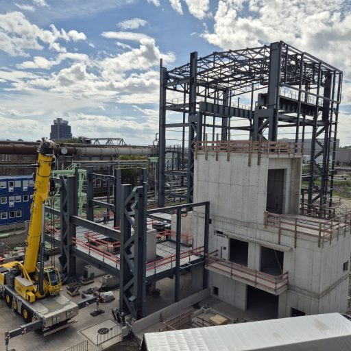 Industriebaustelle mit mehrstöckiger Stahl- und Betonkonstruktion sowie einem Mobilkran bei der Montage der Tragstruktur.