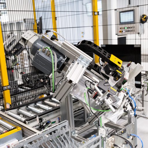 Automated industrial system with robotic or testing unit, conveyor rollers, and safety fencing in a modern production environment.