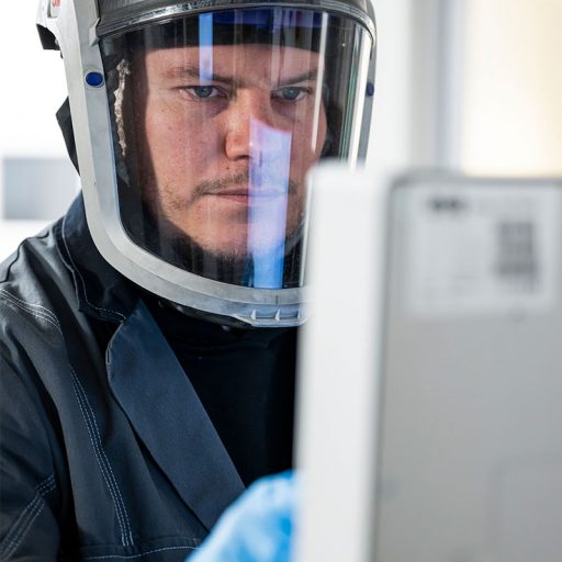 Detailaufnahme auf Bastians Gesicht mit Schutzhelm: er bedient einen industriellen 3D-Drucker im Additive Manufacturing Center