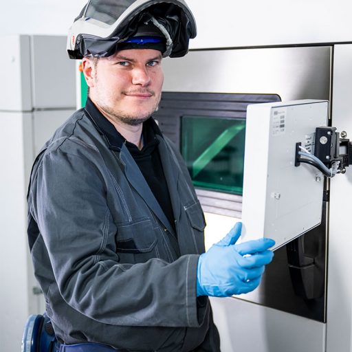 Portraitaufnahme von Bastian beim bedienen eines industriellen 3D-Druckers im Additive Manufacturing Center