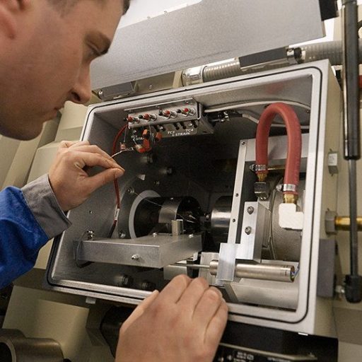 Der voestalpine Mitarbeiter Christian prüft präzise eine Versuchsapparatur zur Werkstoffanalyse im Labor – Fokus auf Forschung und Qualitätsoptimierung.