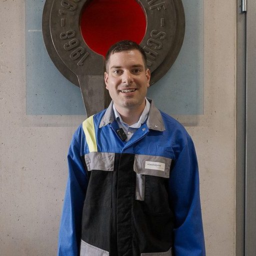 Christian H. from the voestalpine research team stands in workwear in front of a factory wall – ready for his role in material analysis.