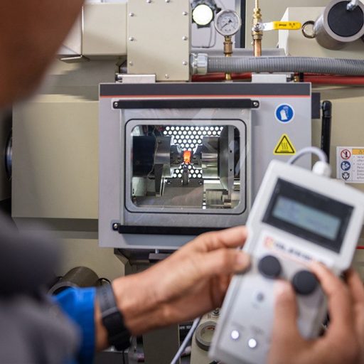 Christian operates a Gleeble testing device using a remote control, examining a heated metal sample inside the chamber.