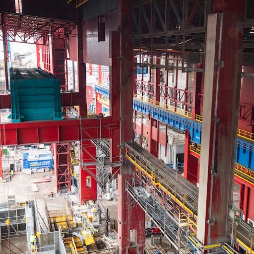 nnenansicht der neuen EAF-Halle der voestalpine im Bau mit roten Stahlträgern, blauen Krananlagen, gelben Geländern und sichtbaren Montagebereichen auf mehreren Ebenen.