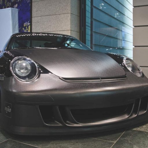 Front view of a black sports car featuring carbon-fiber-look body components at an exhibition.