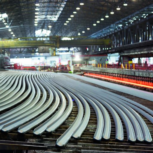 Gebogene Stahlschienen in einer Produktionshalle während der industriellen Fertigung von Schienen für moderne Bahninfrastruktur.