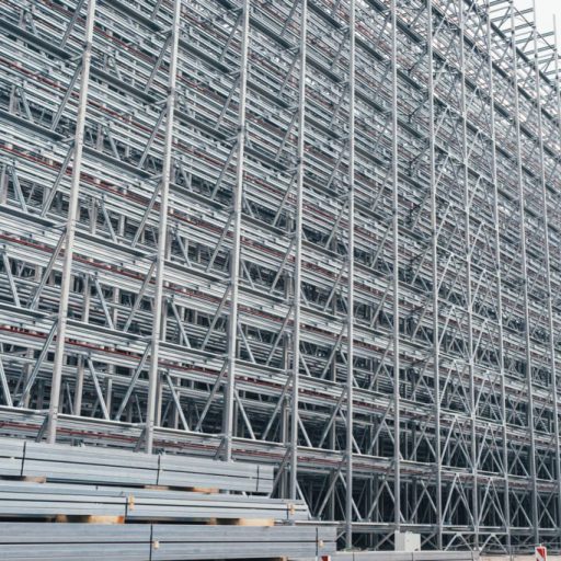 Große Hochregalanlage aus Stahl im Bau mit dicht angeordneten Trägern und gestapelten Stahlprofilen im Vordergrund.