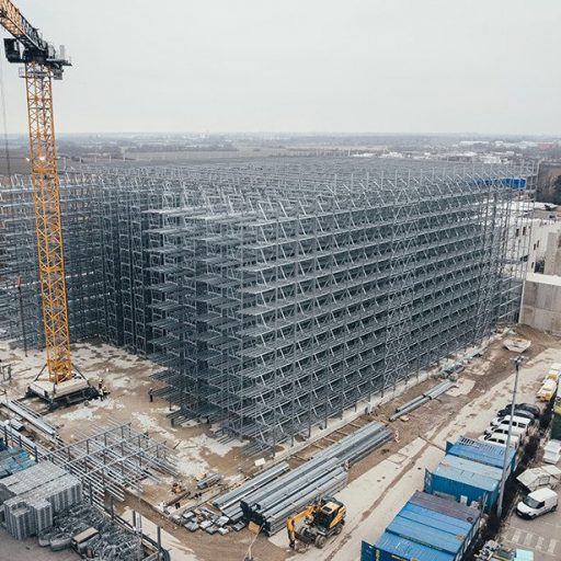 Große Baustelle mit Hochregallager im Bau, Kränen und Baumaterialien, aufgenommen aus der Vogelperspektive.
