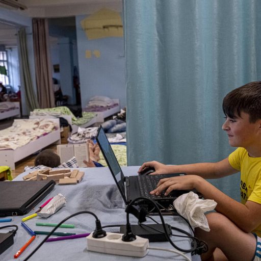 A boy sits at a laptop in a refugee centre