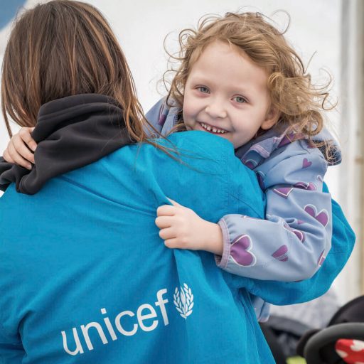 A girl laughs into the camera and is held by a unicef employee who has her back to the camera