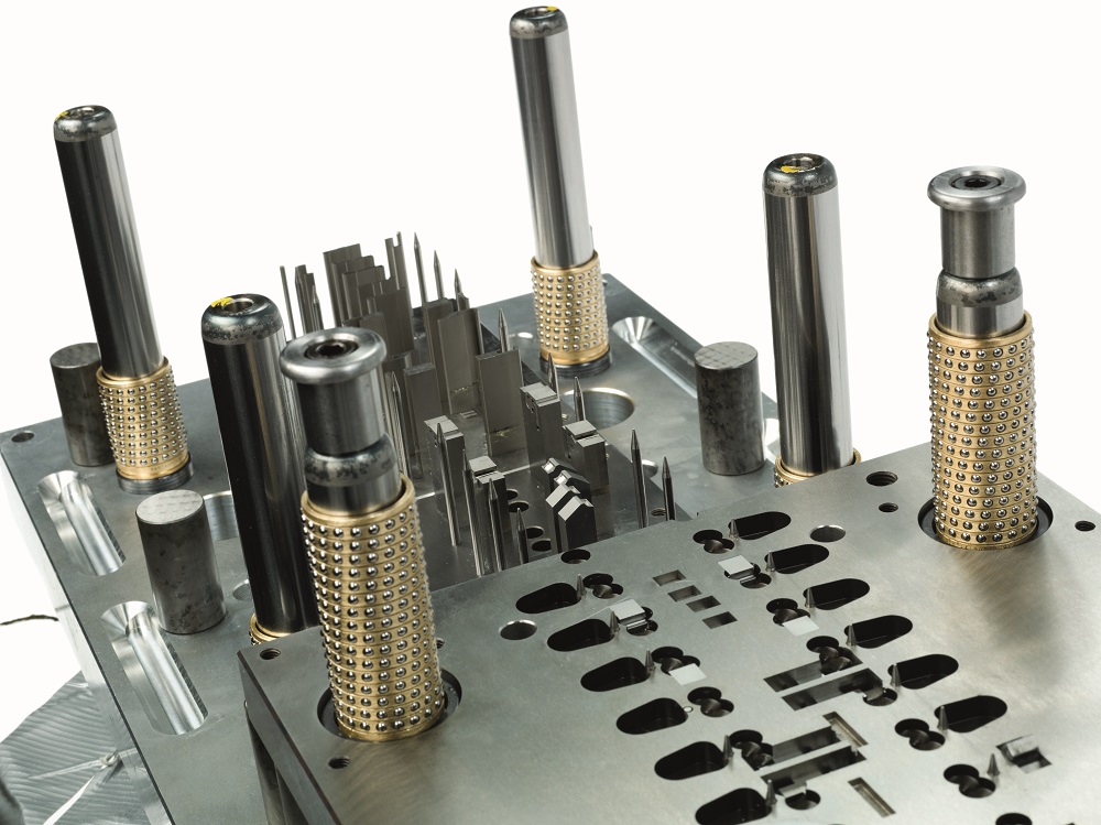 A close-up view of a precision metal mold with cylindrical guide pins and intricate cutouts, designed for industrial manufacturing, injection molding, or cold work tooling applications.