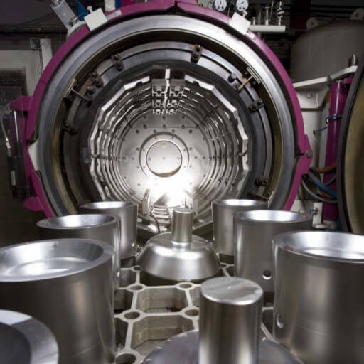 Nahaufnahme des Innenraums einer Industriemaschine, die möglicherweise zur Wärmebehandlung von Stahl und Legierungen verwendet wird, umgeben von zylindrischen Metallteilen in einer Laborumgebung.