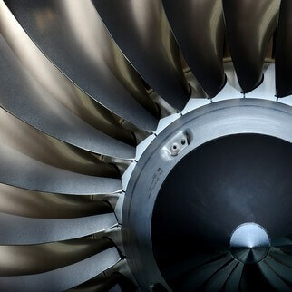 Close-up view of the metallic fan blades inside a jet engine, made for special steel applications e.g. aerospace, arranged in a circular pattern around a central cone, reflecting light and showing intricate details of their smooth surfaces.