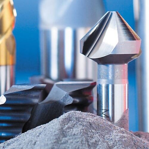 Eine Nahaufnahme verschiedener Bohrer und Schneidwerkzeuge aus Schnellarbeitsstahl mit scharfen Kanten und Rillen, die aufrecht in einem Haufen grauer Metallspäne vor einem blauen Hintergrund stehen.