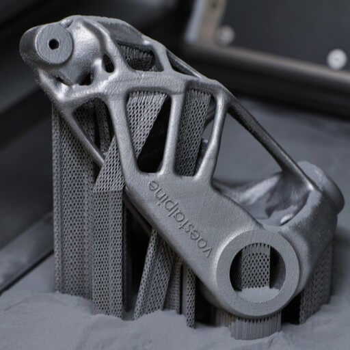 Close-up of two metal 3D-printed parts with intricate geometric designs, partially embedded in a powder bed, highlighting detailed support structures created by the additive manufacturing process.