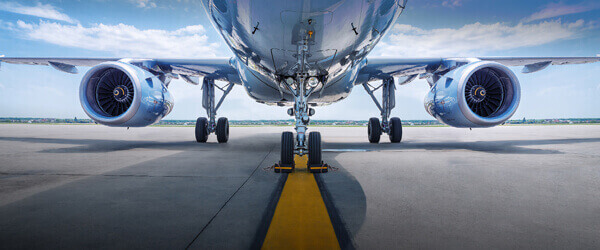 A close-up, front view of a commercial airplane on the runway, showing its nose, landing gear, and two engines under a blue sky with scattered clouds.