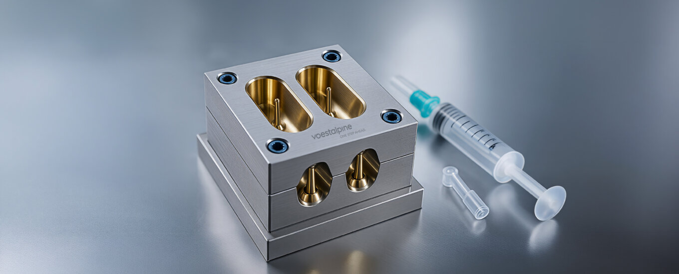 A metal injection mold with four cavities PVD Coated is displayed on a reflective surface beside a plastic syringe and a small transparent cap.