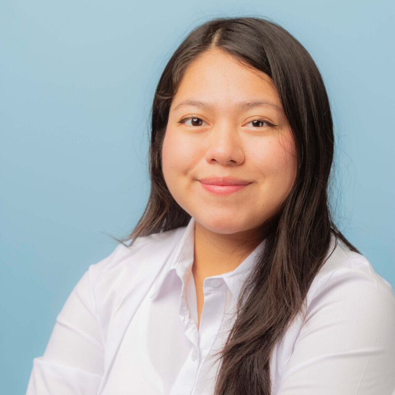 A woman with long hair wearing a white shirt looks thoughtfully ahead, inviting contacto with her calm presence.