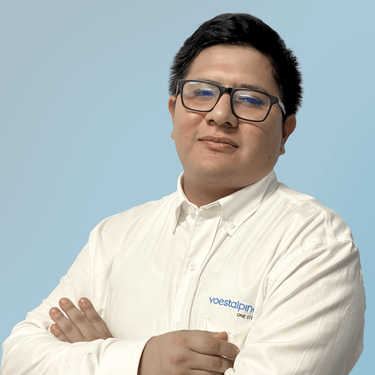 A man with short dark hair and glasses, wearing a white button-up shirt with the voestalpine logo, stands with arms crossed against a light blue background, conveying confidence and análisis.
