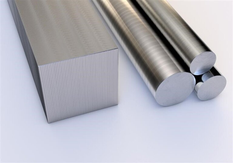 Three metal rods with a smooth, shiny surface are placed next to a large rectangular metal bar with a brushed texture, all resting on a light-colored surface.